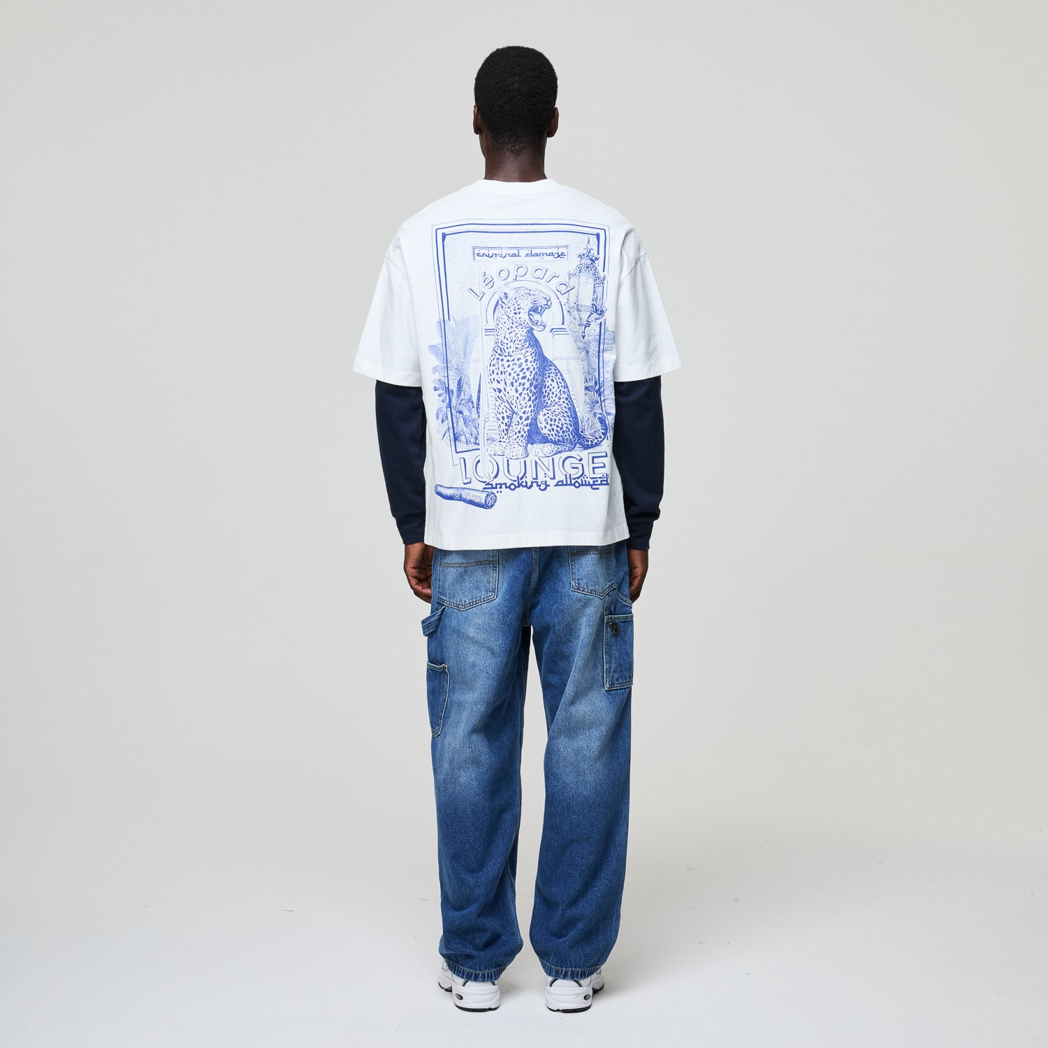 Person wearing a white t-shirt with blue graphics and text, standing against a plain background