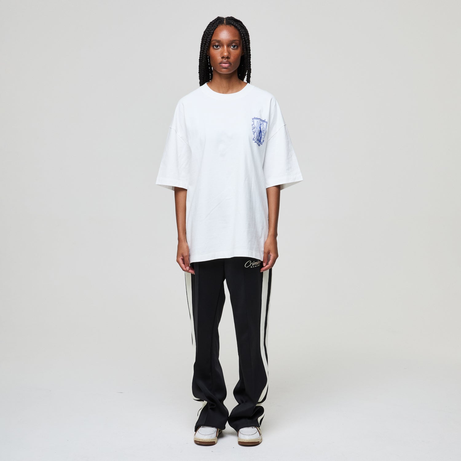 Person wearing a white oversized t-shirt and black pants with a stripe on a plain background