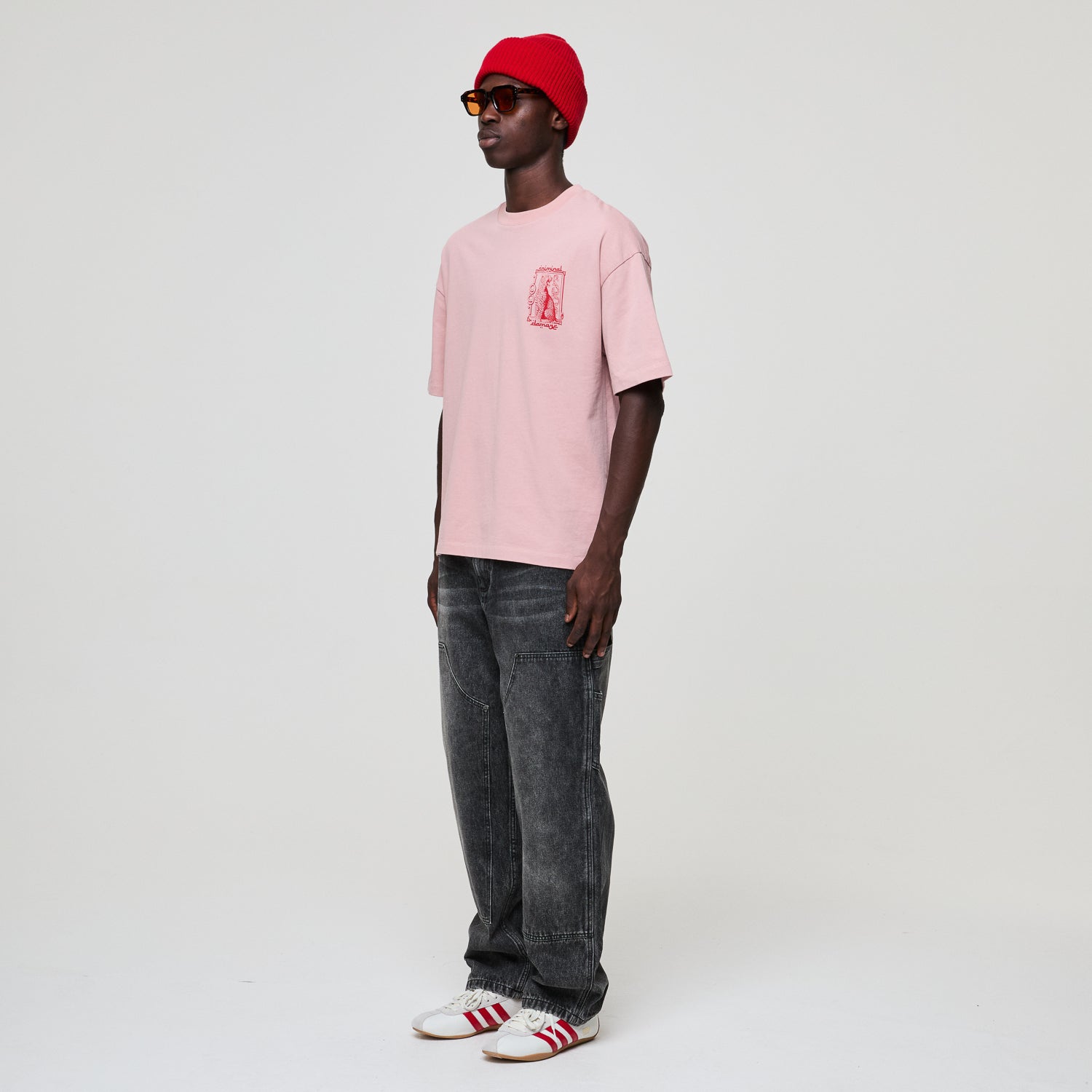 Person wearing a pink t-shirt, red beanie, and gray jeans on a white background