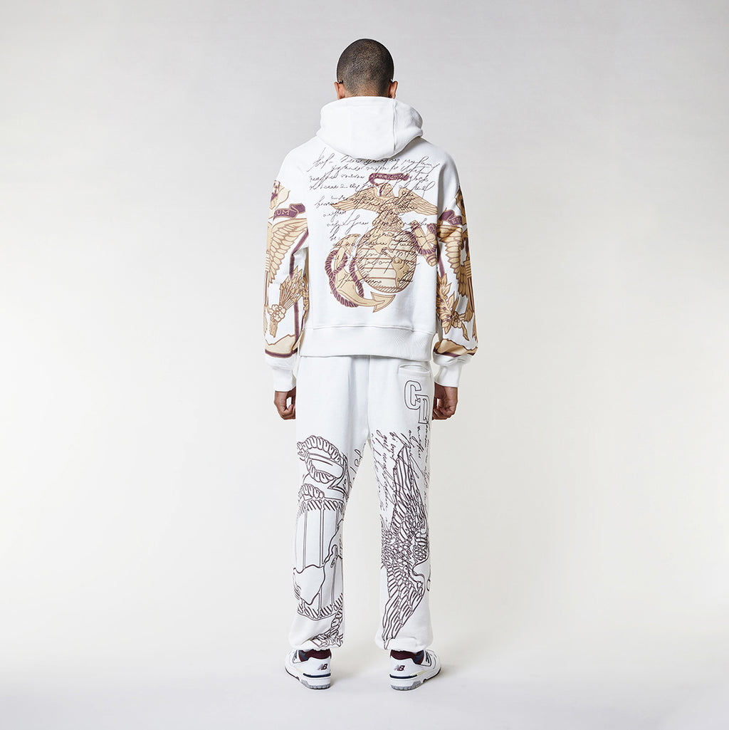 Man wearing a Criminal Damage white hoodie with graphic designs on a plain background