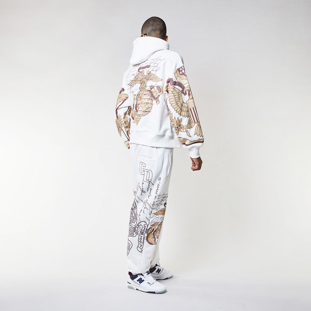 Man wearing a Criminal Damage white hoodie with graphic designs on a plain background