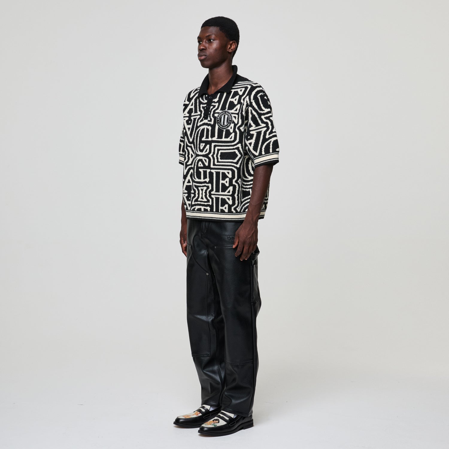 Person wearing a black and white patterned shirt with black leather pants on a white background