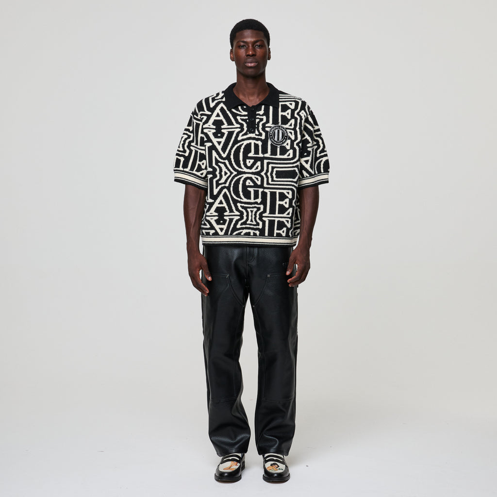 Person wearing a black and white patterned shirt with text, standing against a plain background