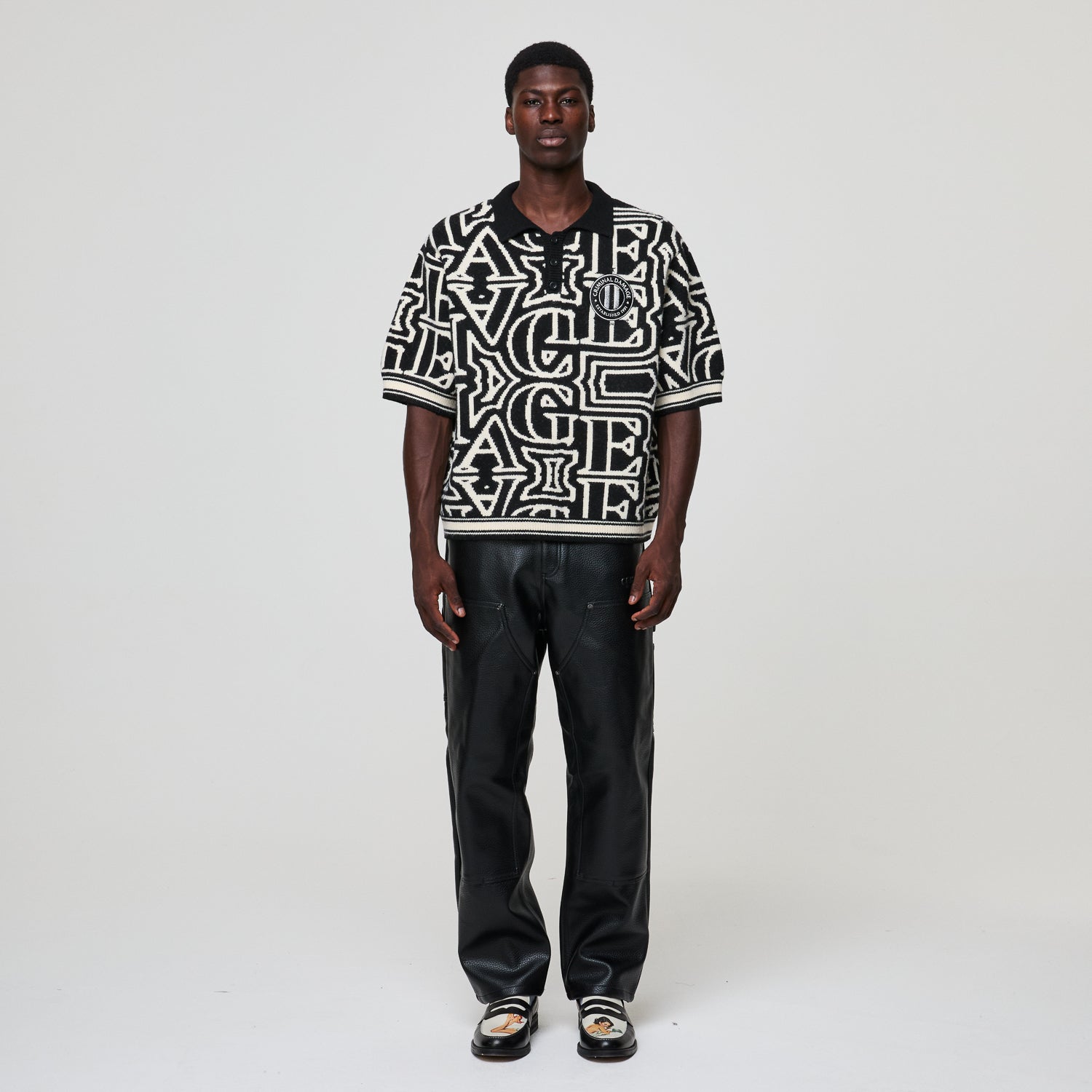 Person wearing a black and white patterned shirt with text, standing against a plain background