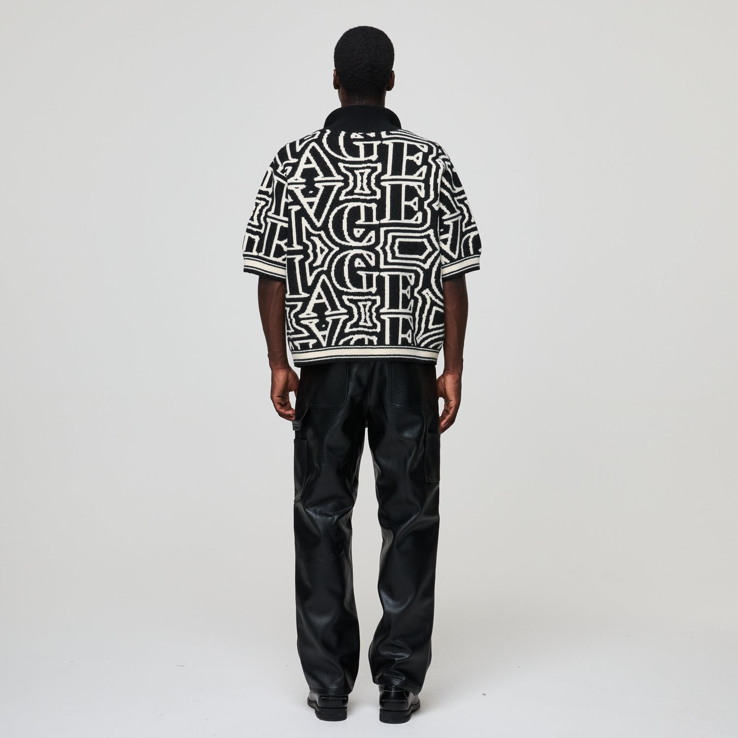 Person wearing a black and white patterned shirt with black pants on a white background
