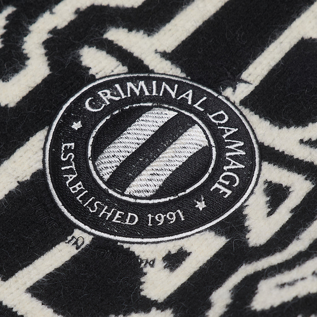 Close-up of a 'Criminal Damage' logo on a black and white patterned background