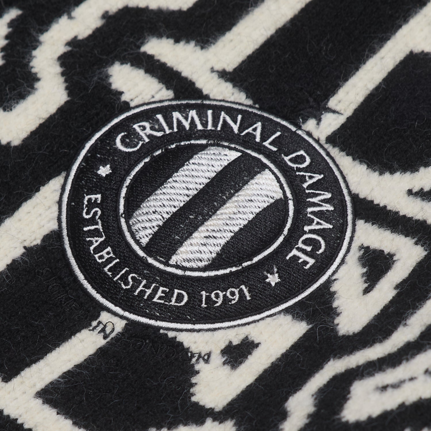 Close-up of a 'Criminal Damage' logo on a black and white patterned background