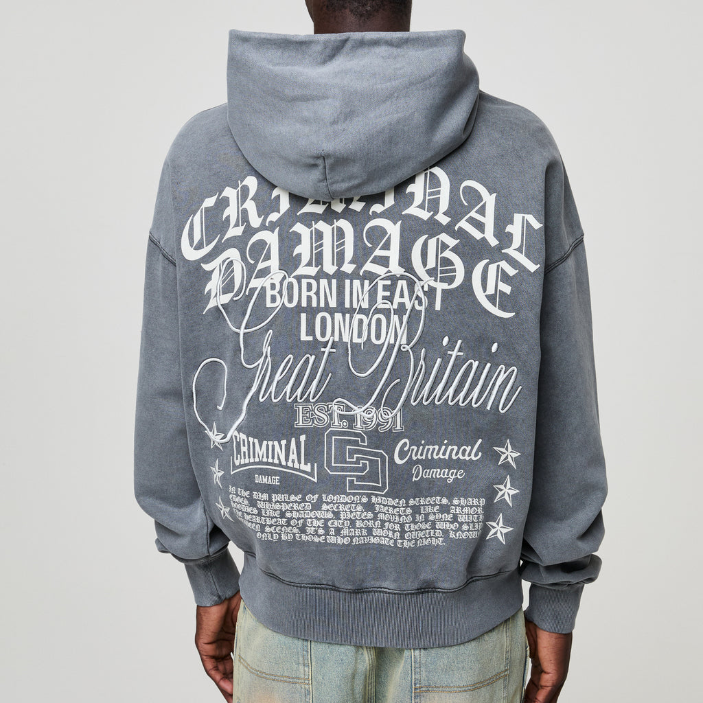 Gray Criminal Damage hoodie with white text on the back, worn by a person against a plain background