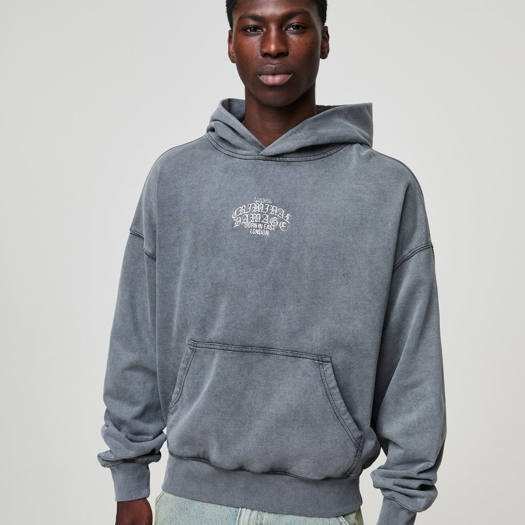 Person wearing a gray Criminal Damage hoodie with a logo on a plain background