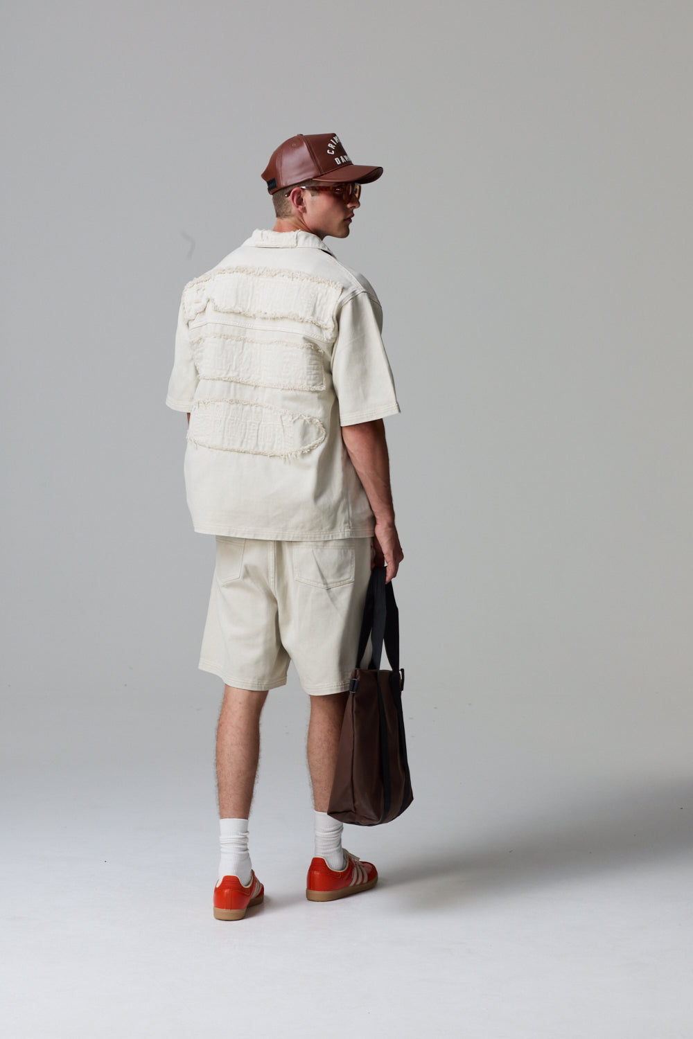 Model wearing a Criminal Damage cotton white outfit with a brown bag on a grey background