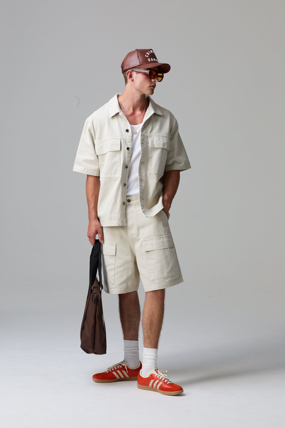Model wearing a Criminal Damage cotton beige shirt, shorts, and red sneakers with a grey background