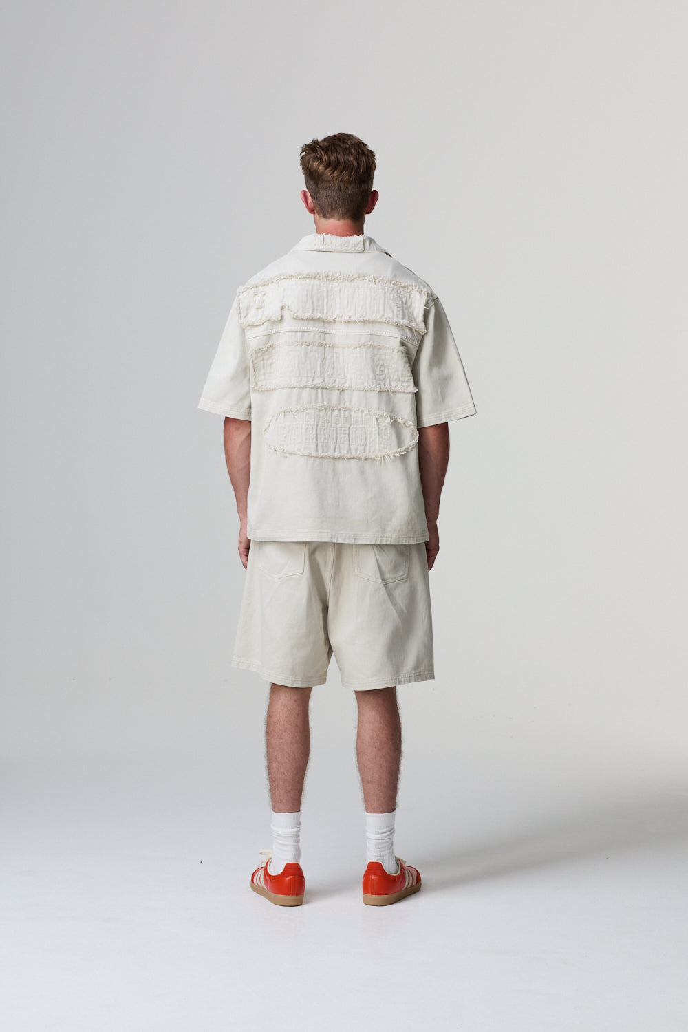 Model wearing a Criminal Damage layered outfit with a white shirt and beige shorts on a grey background
