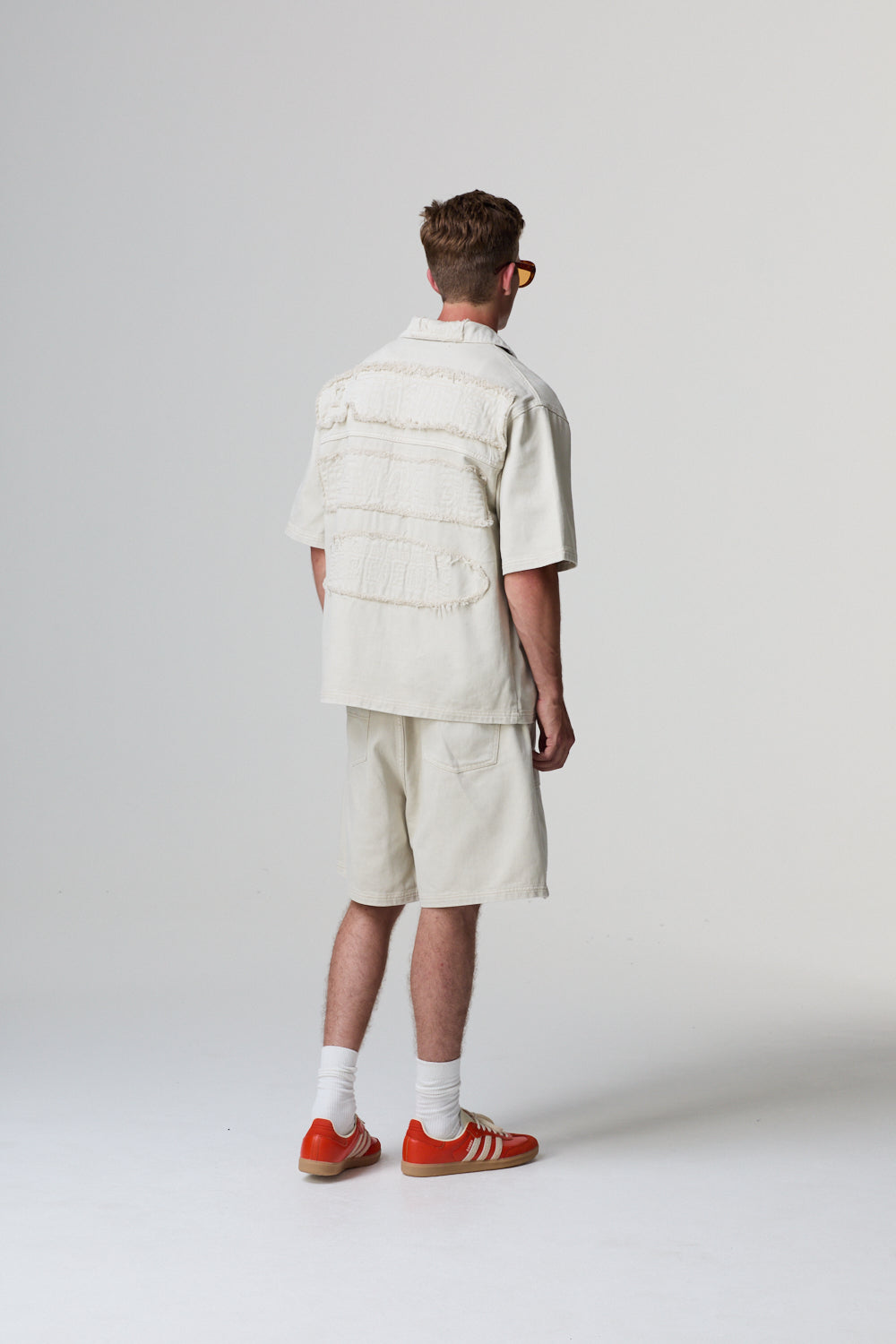 Model wearing a Criminal Damage cotton white outfit with red shoes on a grey background