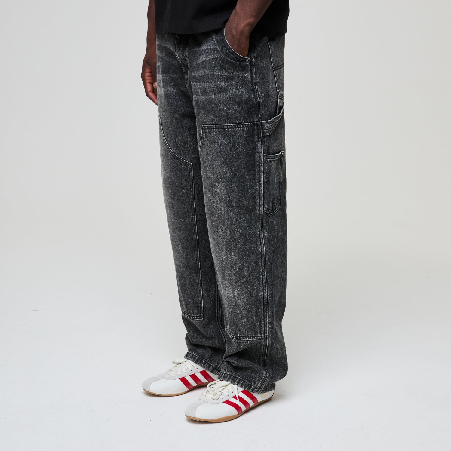 Person wearing black acid-wash jeans and white sneakers with red stripes on a light gray background