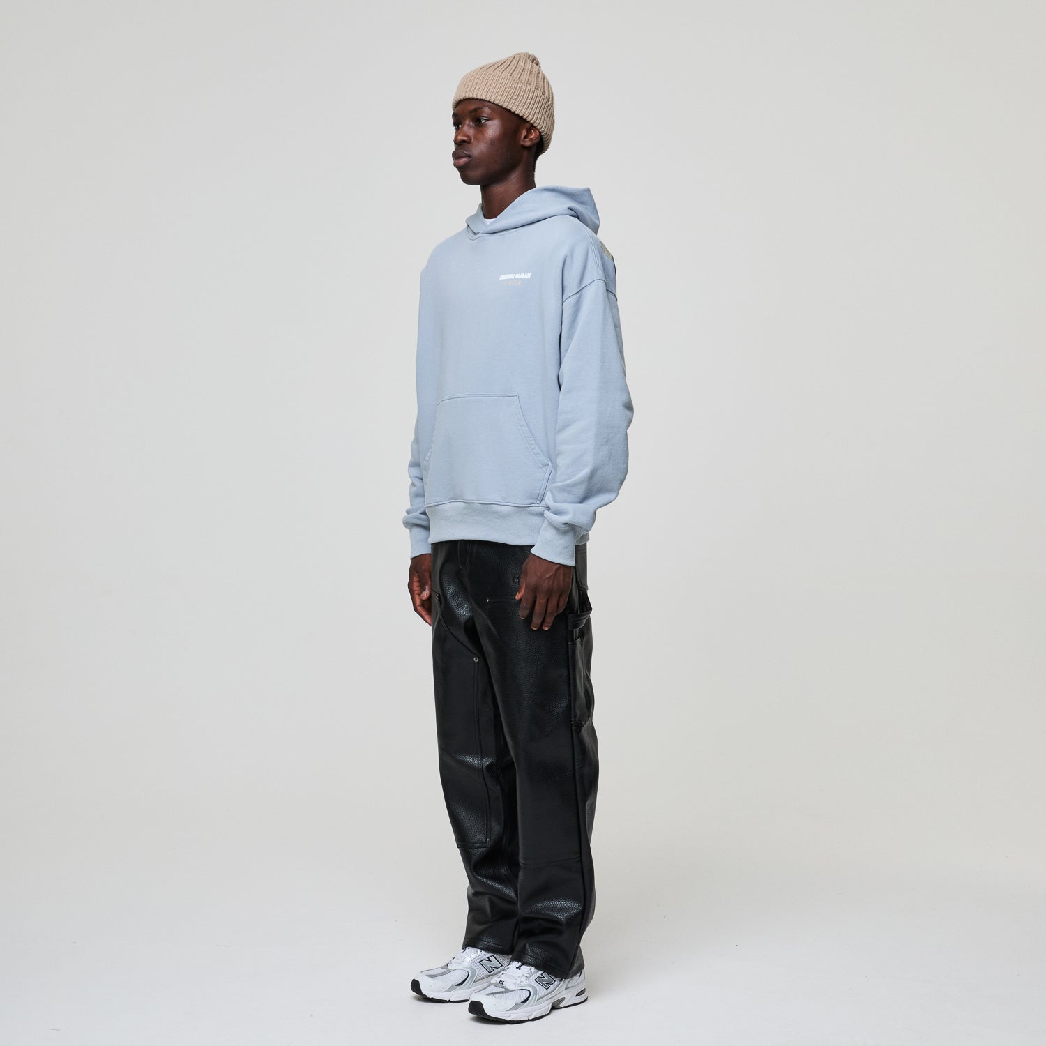Model wearing a Criminal Damage light blue hoodie, black pants, and a beige beanie on a white background