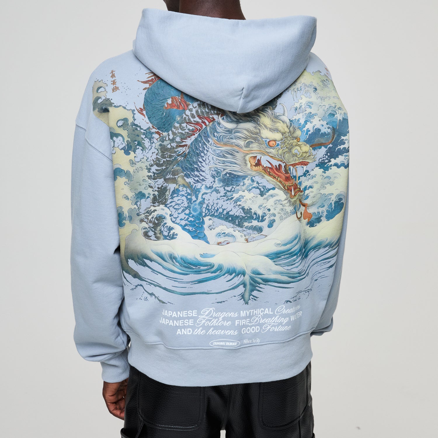 Light blue Criminal Damage hoodie with a dragon design on the back, worn by model.