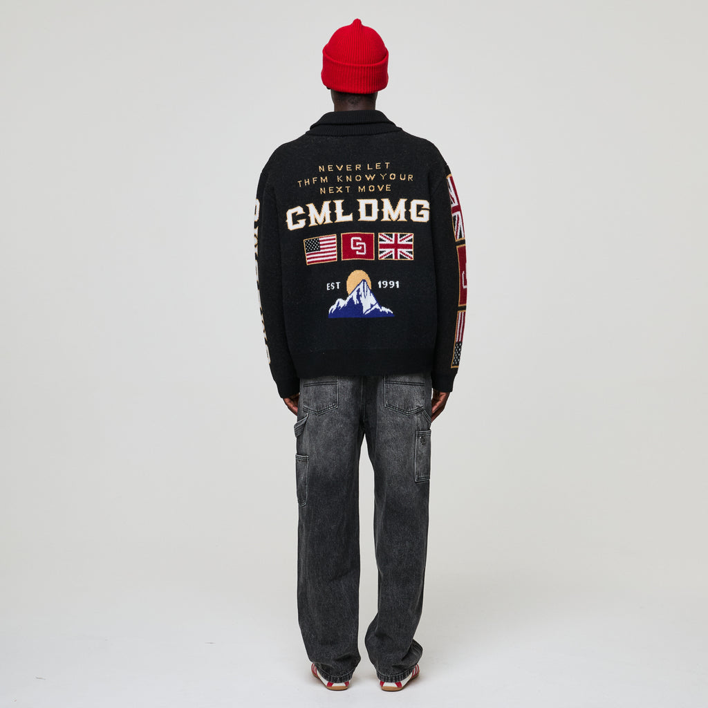 Person wearing a Criminal Damage black jacket with text and graphics on the back, standing against a plain background
