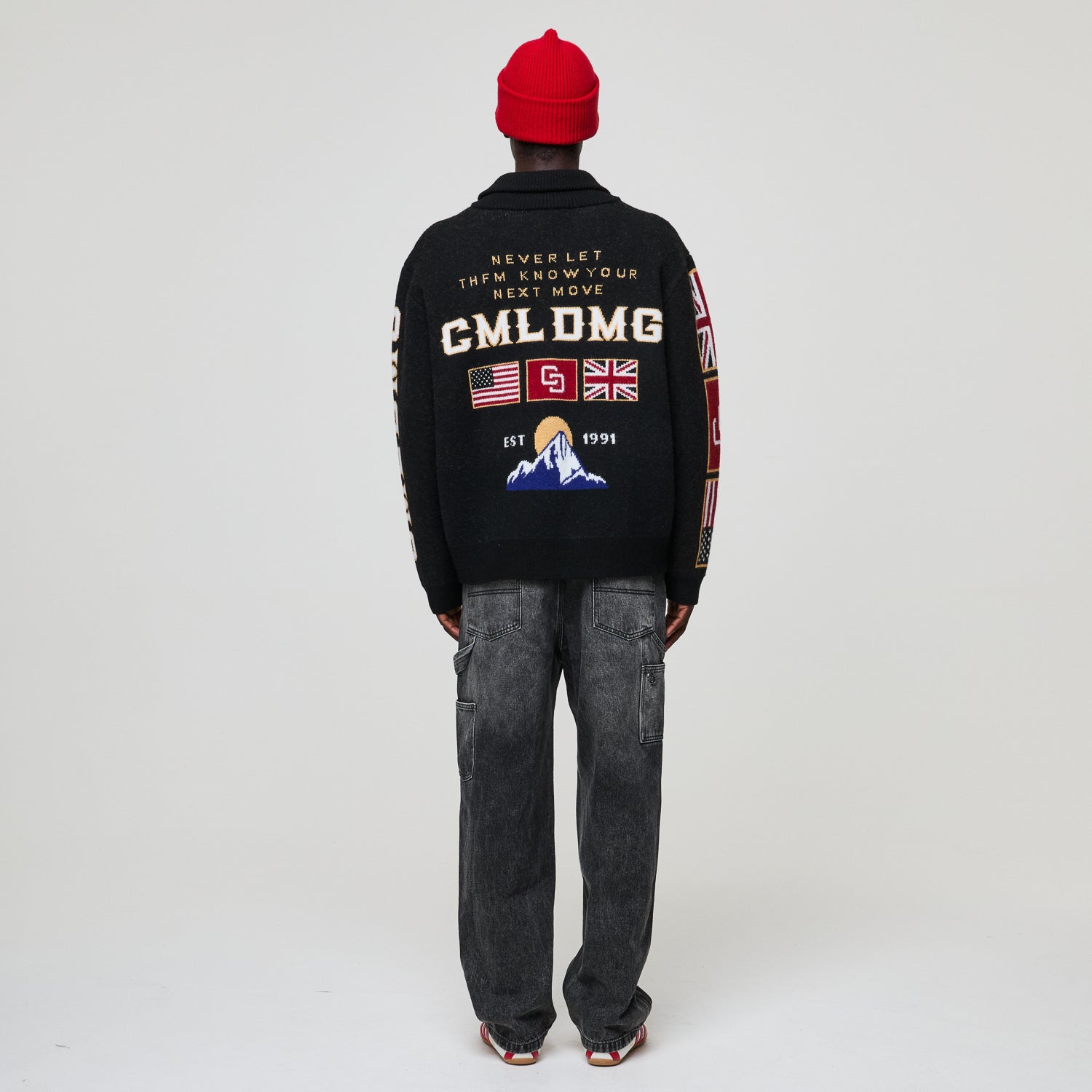 Person wearing a Criminal Damage black jacket with text and graphics on the back, standing against a plain background