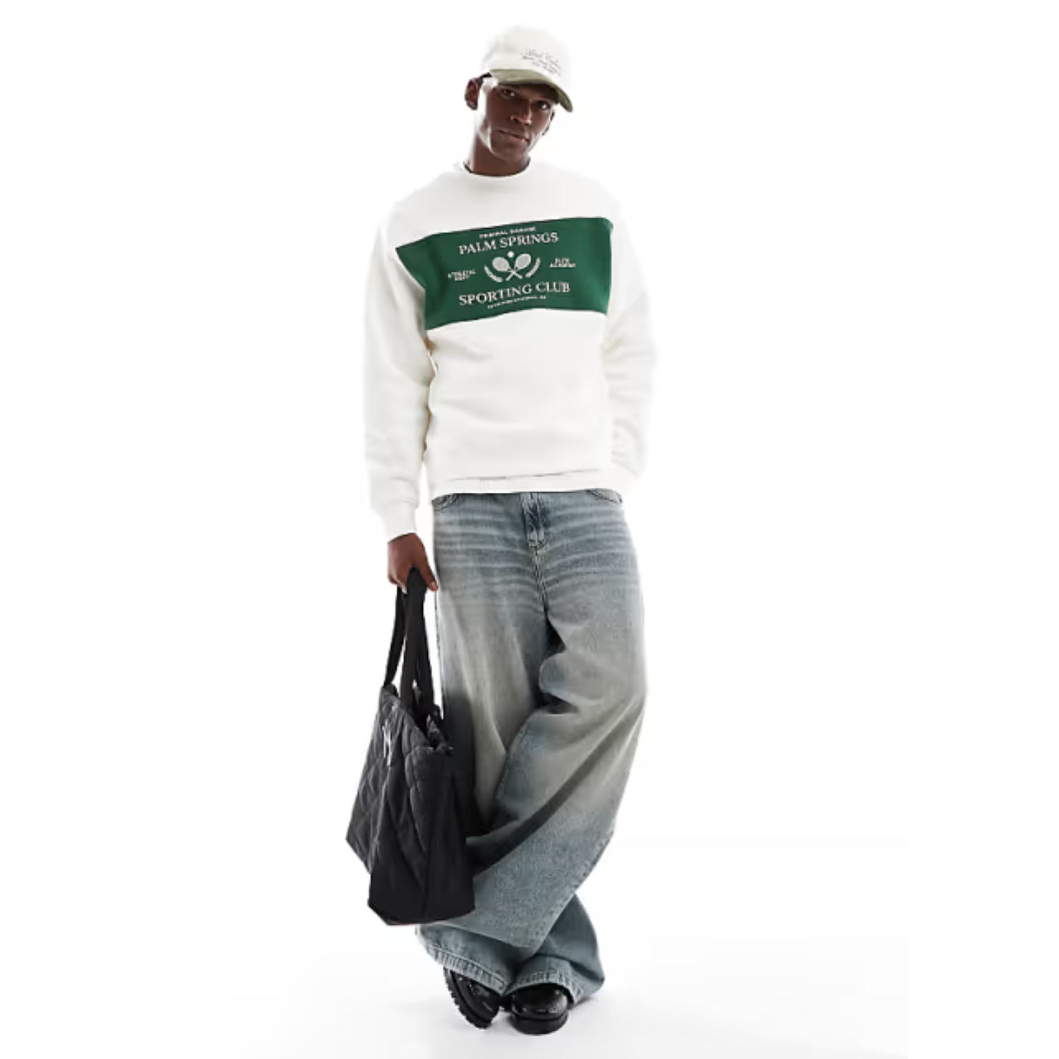 Person wearing a white sweatshirt with a logo and gray jeans, holding a black bag on a white background