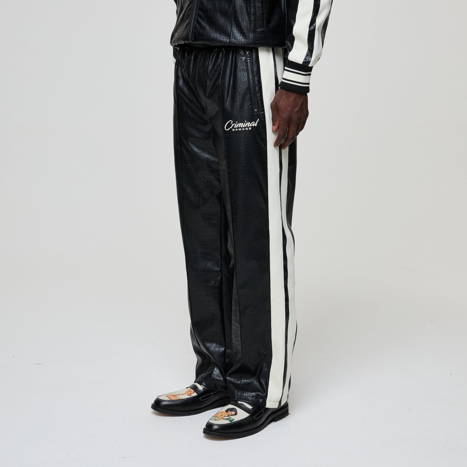 Black leather track pants with white stripe and 'Criminal' branding on a white background
