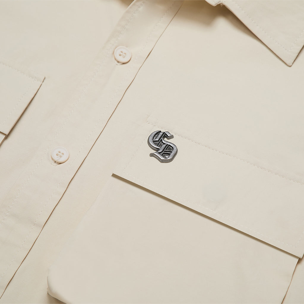 Close-up of a beige shirt with a logo on the chest pocket.