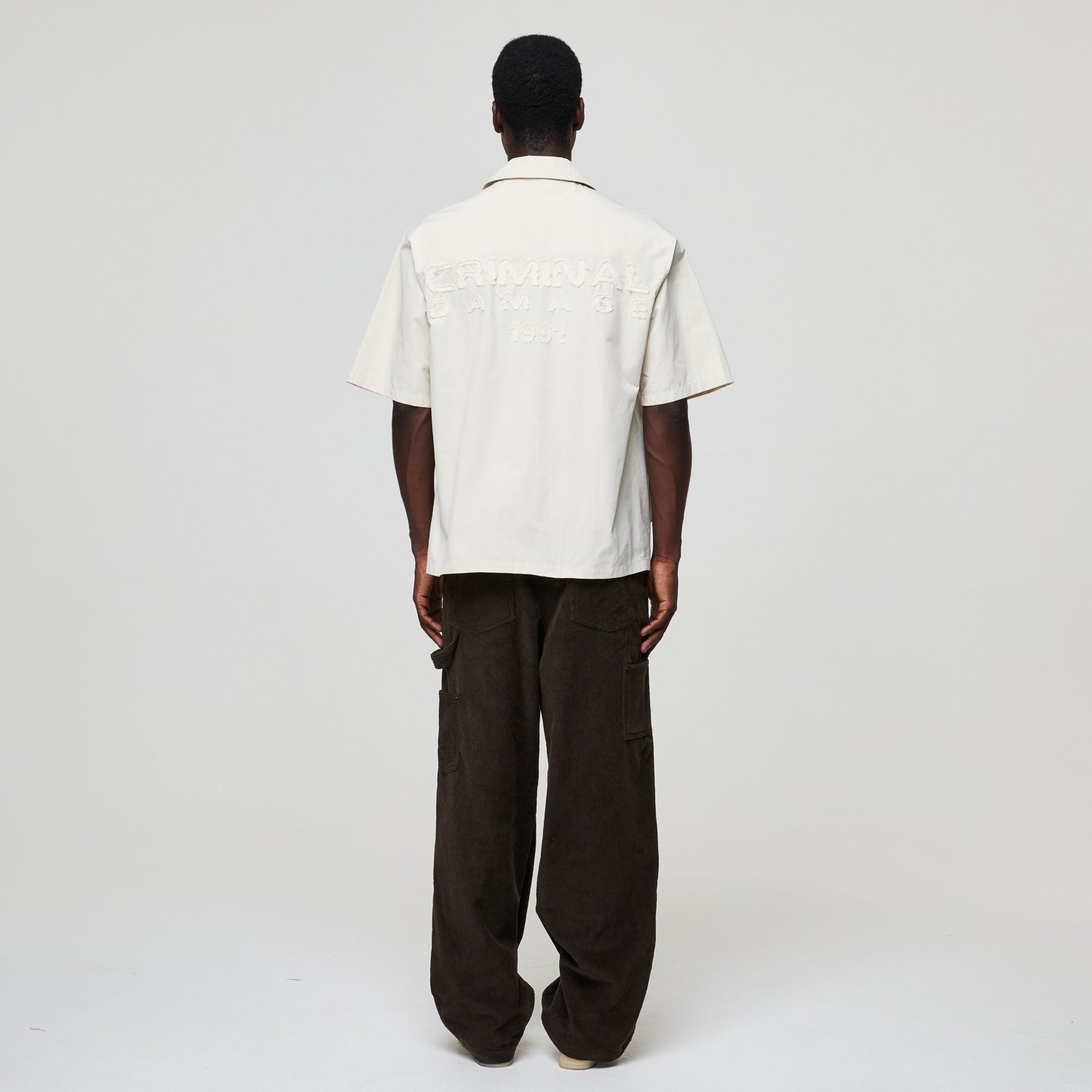 Person wearing a white shirt and dark pants on a plain background