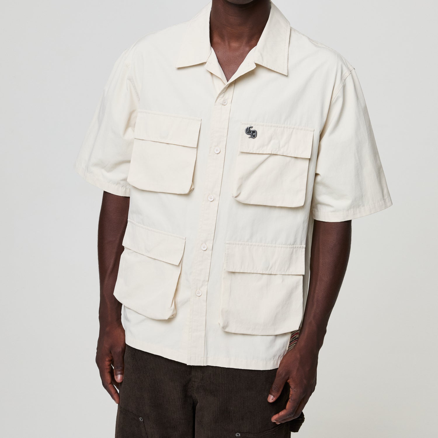 Person wearing a beige short-sleeve shirt with multiple pockets on a plain background