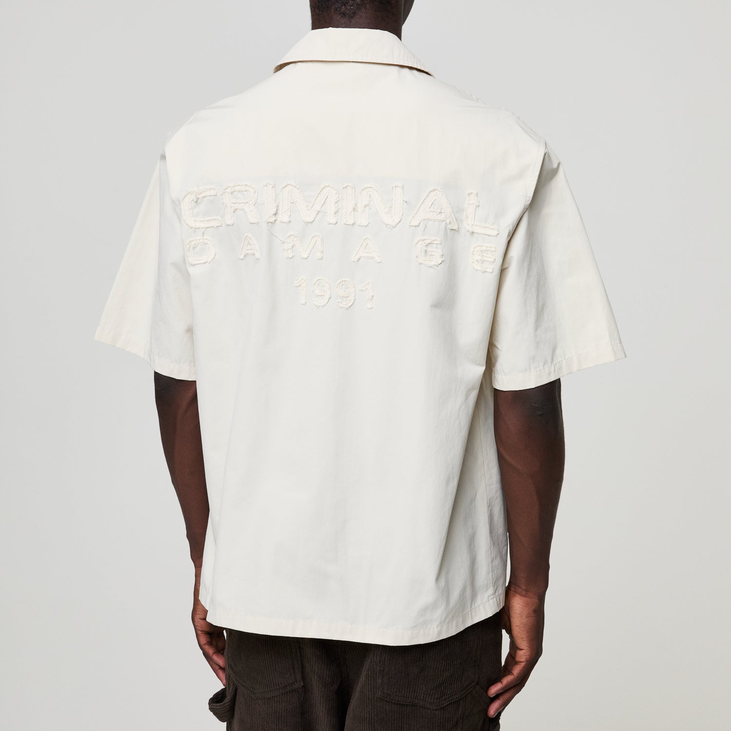 White shirt with text on the back worn by a person against a gray background