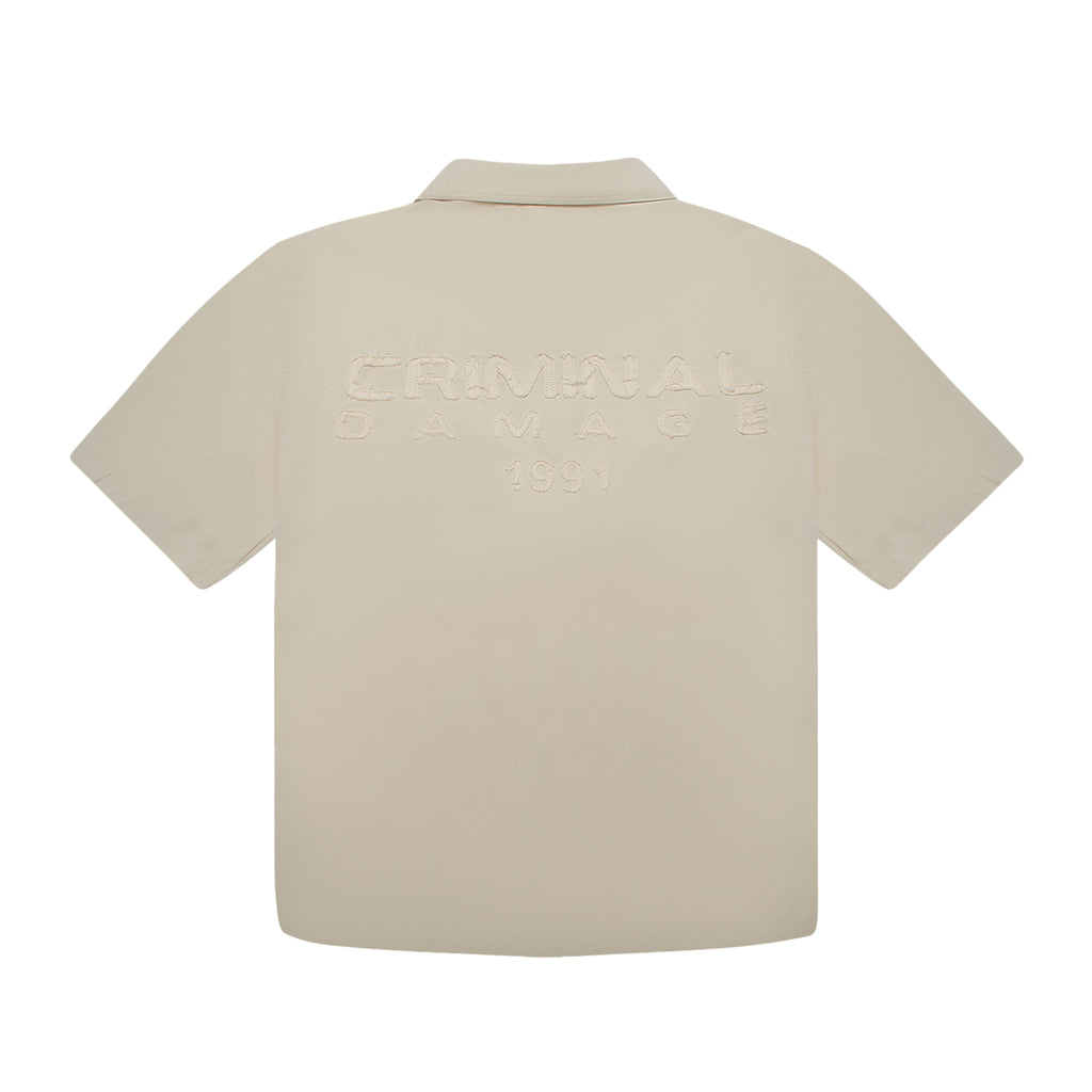 Beige polo shirt with 'Criminal Damage' branding on a white background