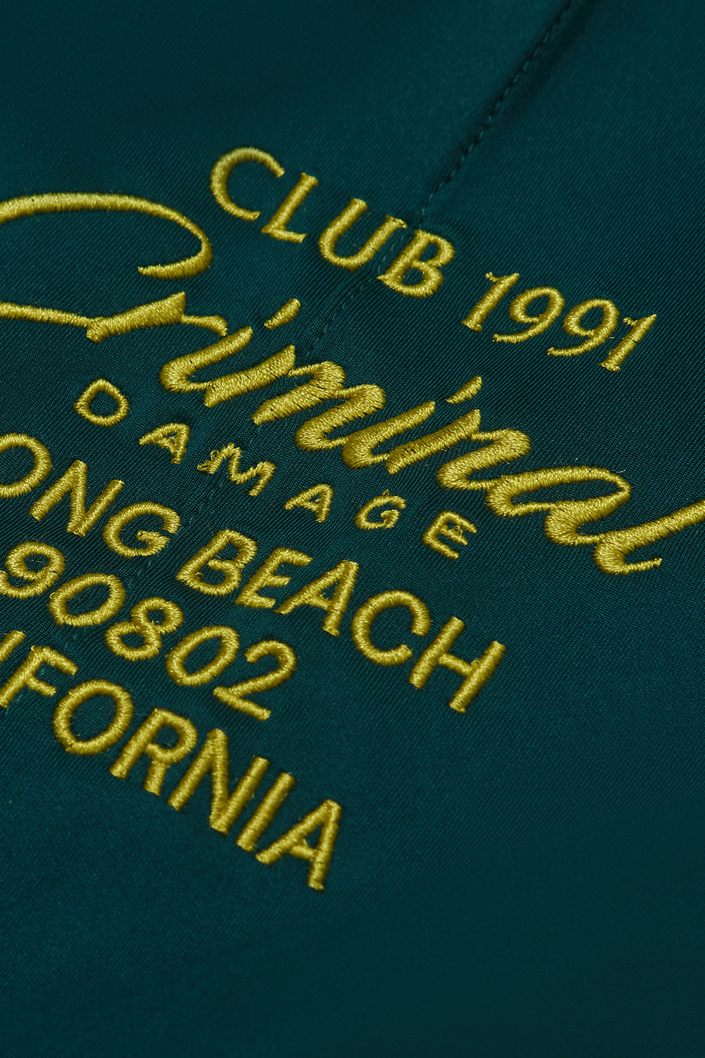 Criminal Damage textured green fabric with yellow embroidered text 