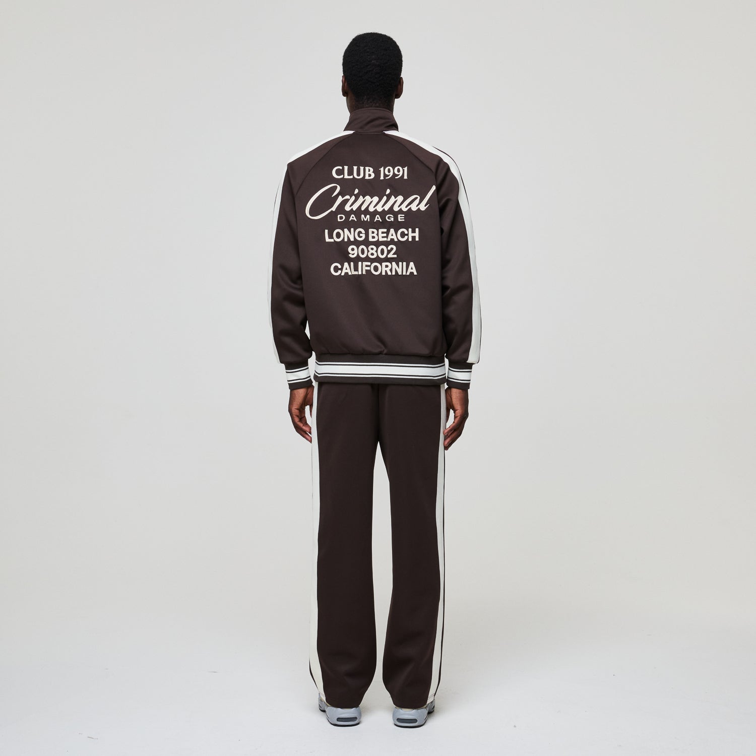 Person wearing a black tracksuit with white text on the back against a white background