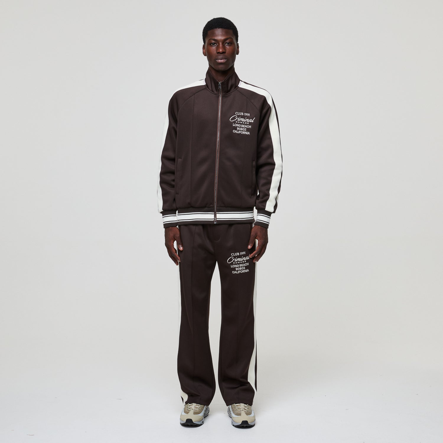 Man wearing a brown tracksuit with white stripes on a white background