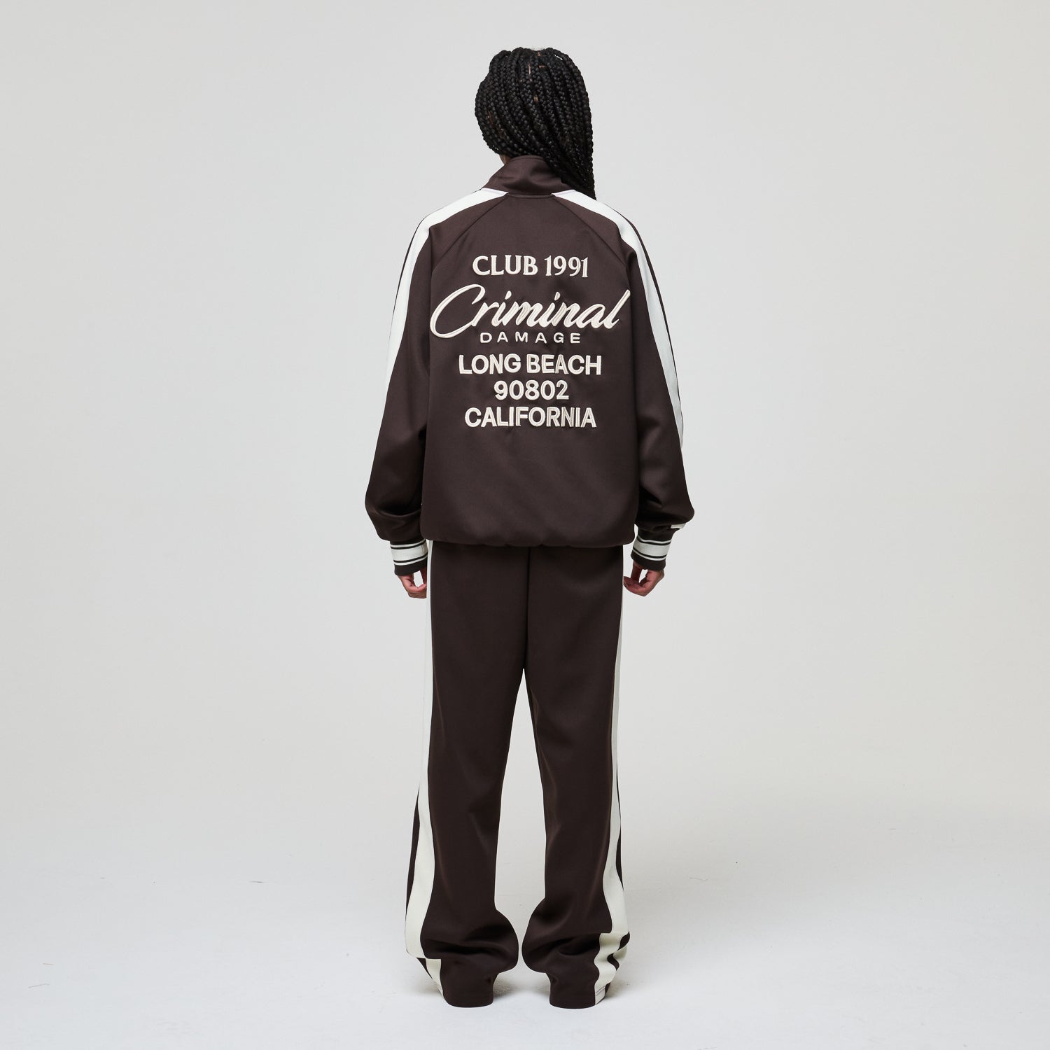Person wearing a black tracksuit with white text on the back against a gray background