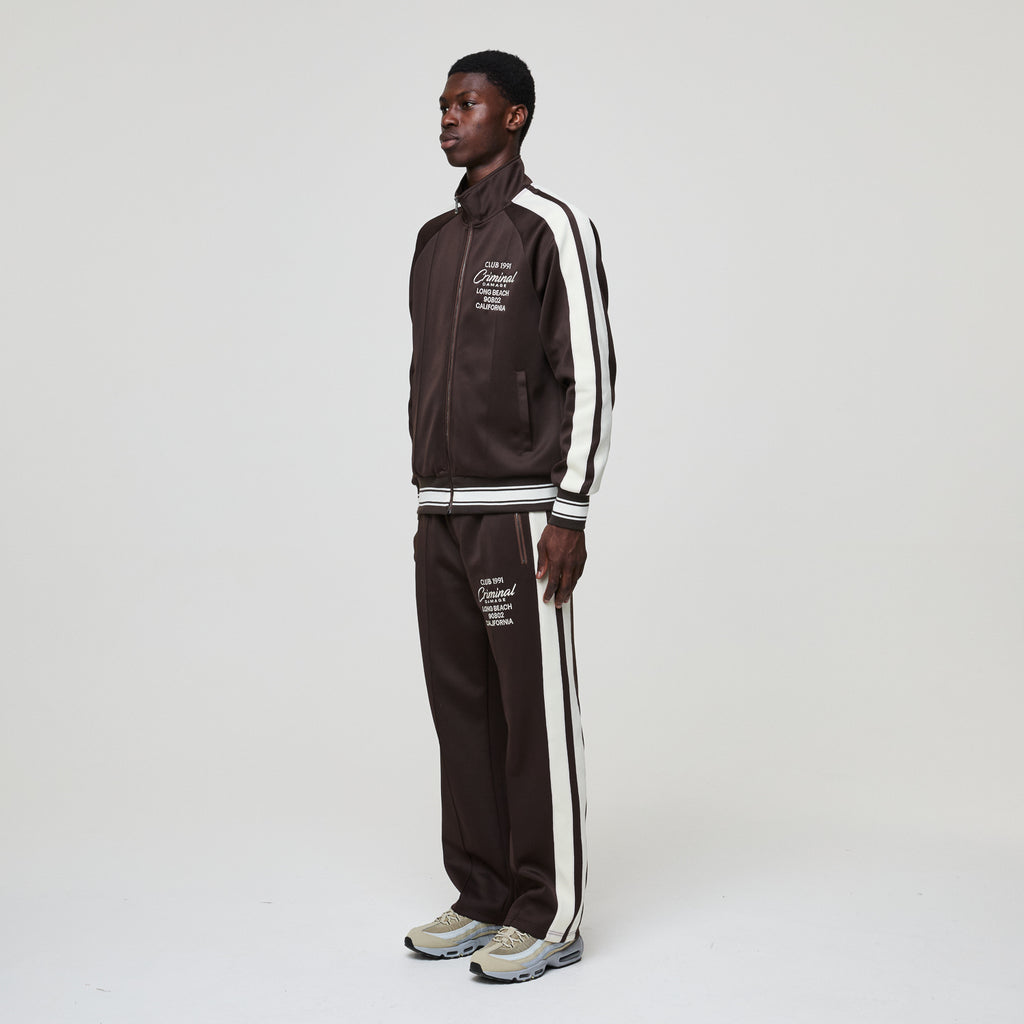 Person wearing a brown tracksuit with white stripes on a white background