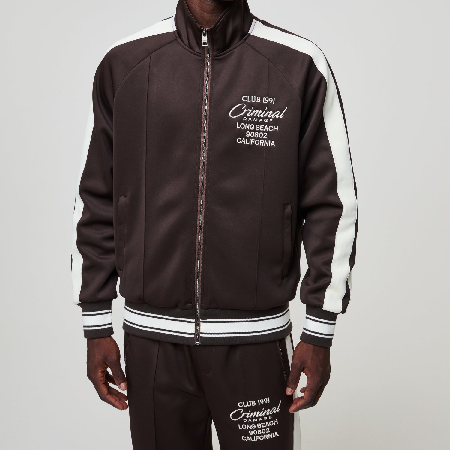 Brown tracksuit with white accents and visible branding on a gray background