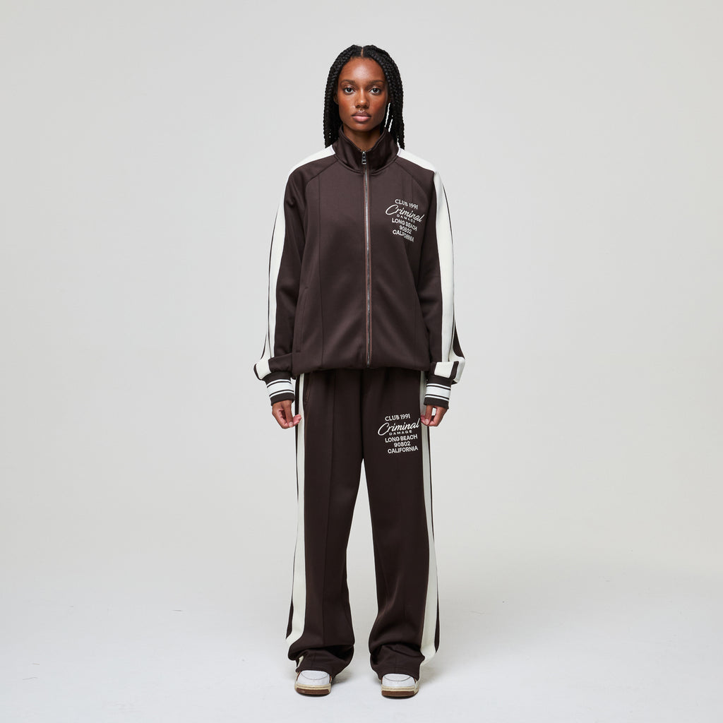 Person wearing a brown tracksuit with white stripes on a plain background