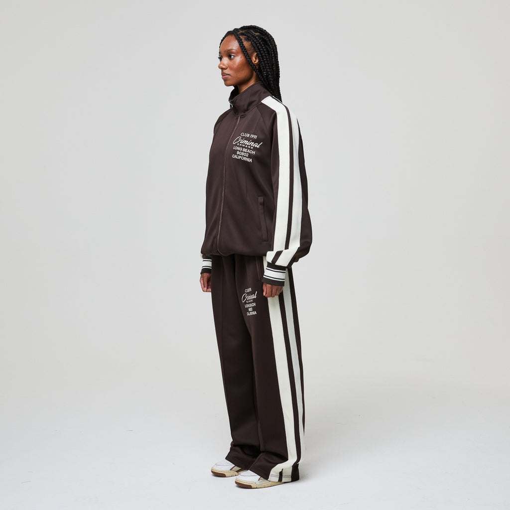 Person wearing a brown tracksuit with white stripes on a light gray background
