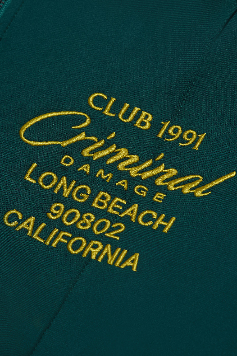 Criminal Damage green hoodie with yellow embroidered text on a dark green background