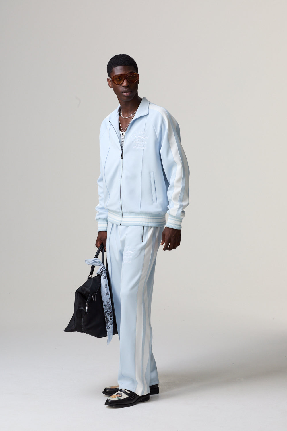 Model wearing a Criminal Damage light blue tracksuit holding a black bag 