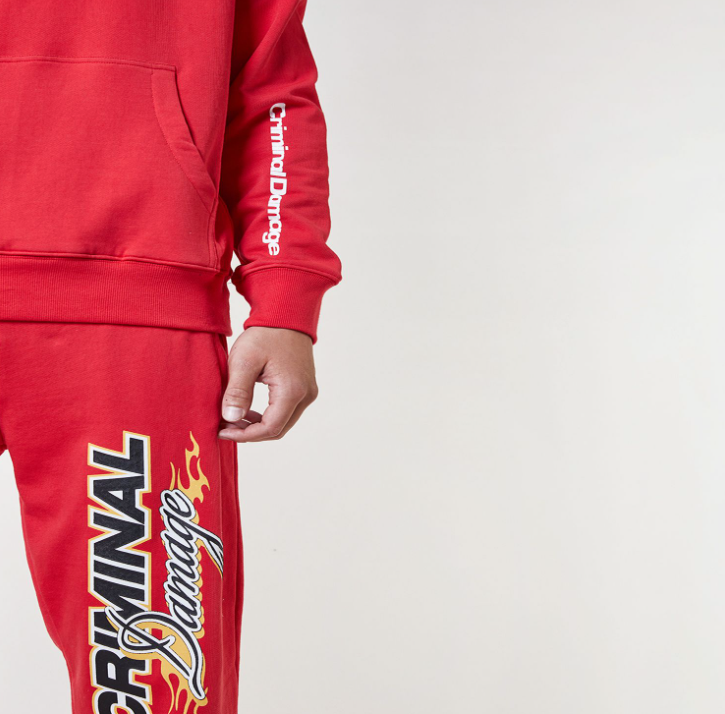 Model wearing a red Criminal Damage hoodie and pants on a white background