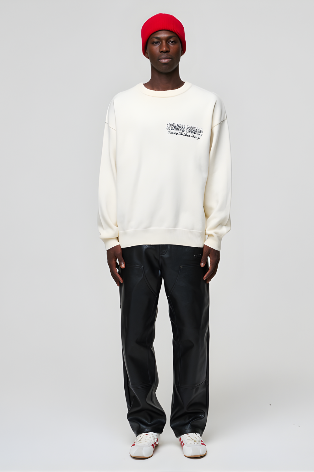 Person wearing a white sweatshirt with text, black pants, and a red beanie on a light gray background