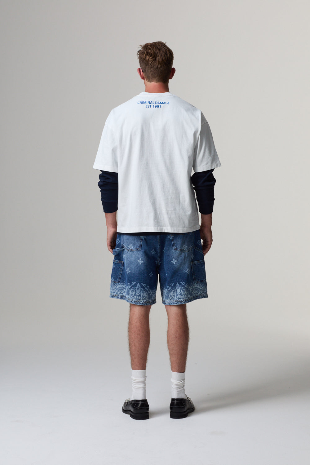 Model wearing a white Criminal Damage t-shirt with text and blue distressed shorts on a grey background