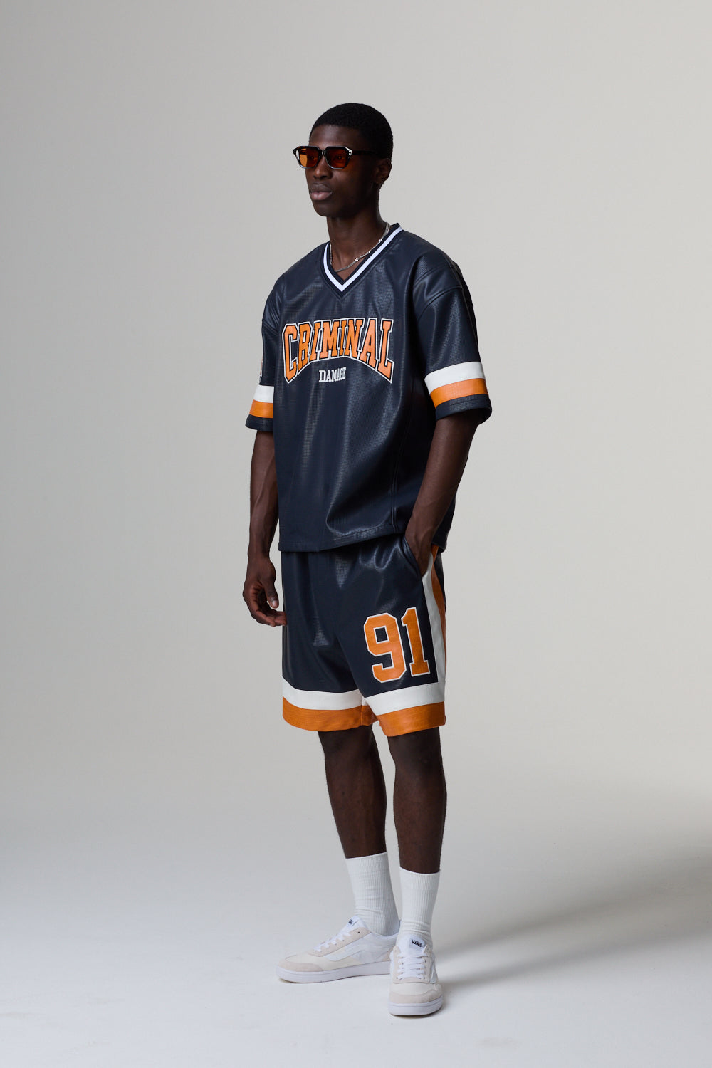 Model wearing a Criminal Damage navy blue sports jersey with orange and white accents on a grey background