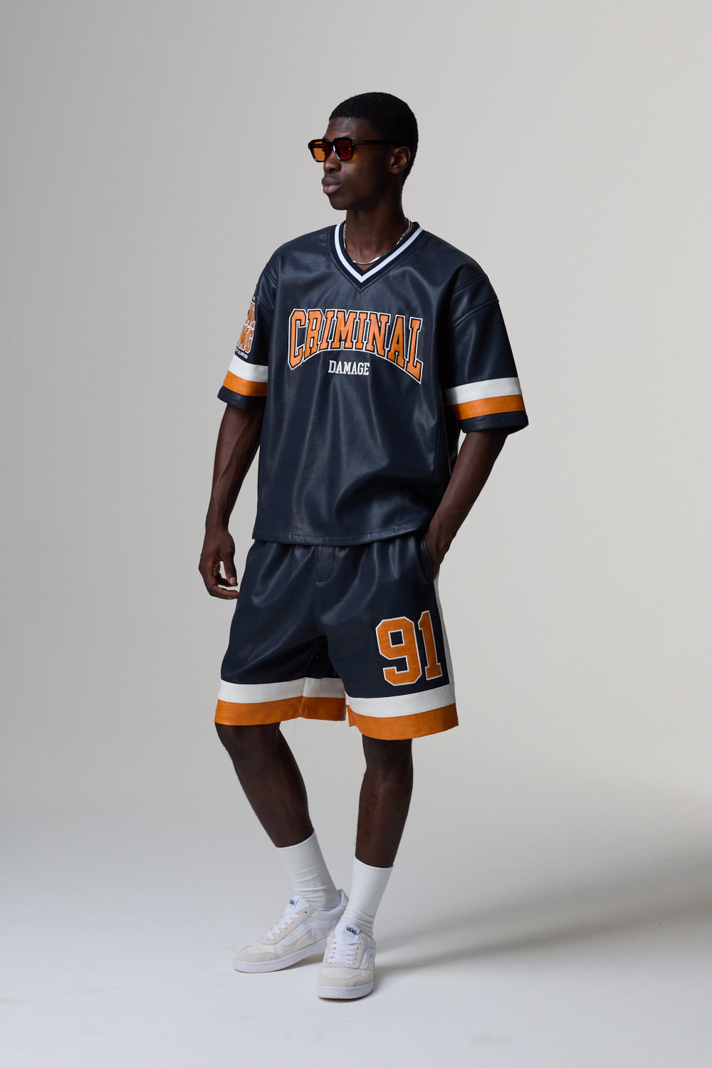 Model wearing a navy blue sports jersey with 'Criminal Damage' and shorts with number '91' on a grey background