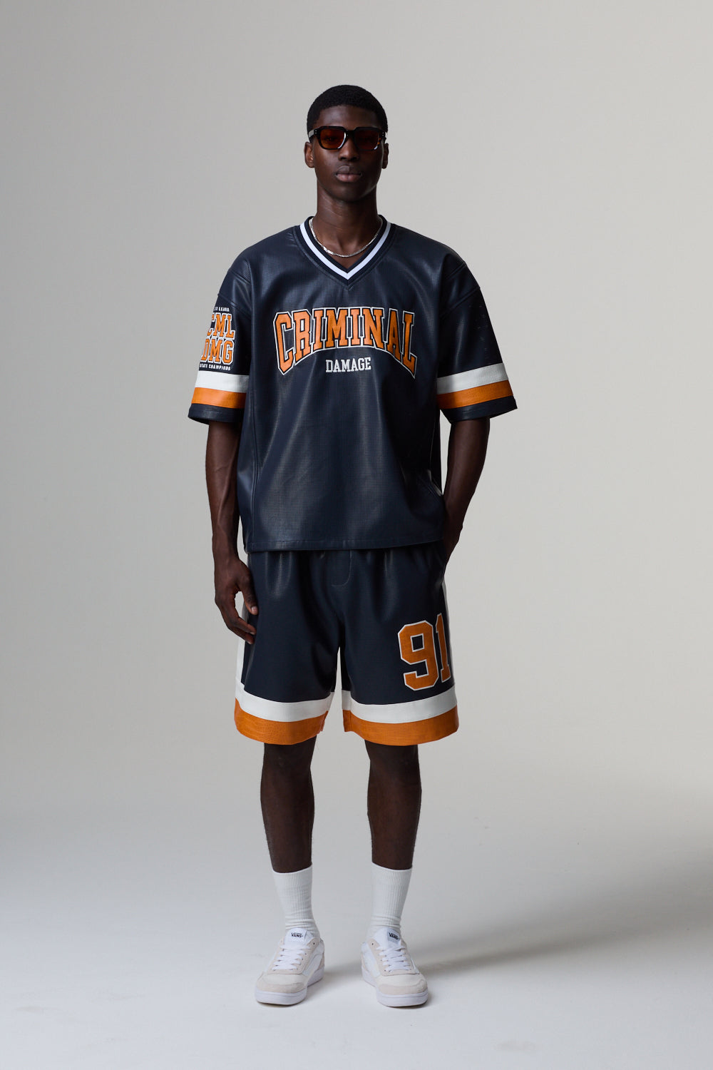 Model wearing a Criminal Damage navy blue sports jersey with orange and white accents on a grey background
