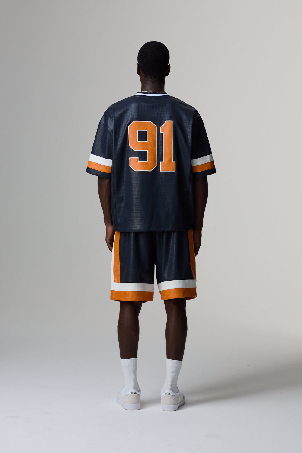 Model wearing a Criminal Damage navy blue sports jersey with orange and white accents, standing against a grey background.