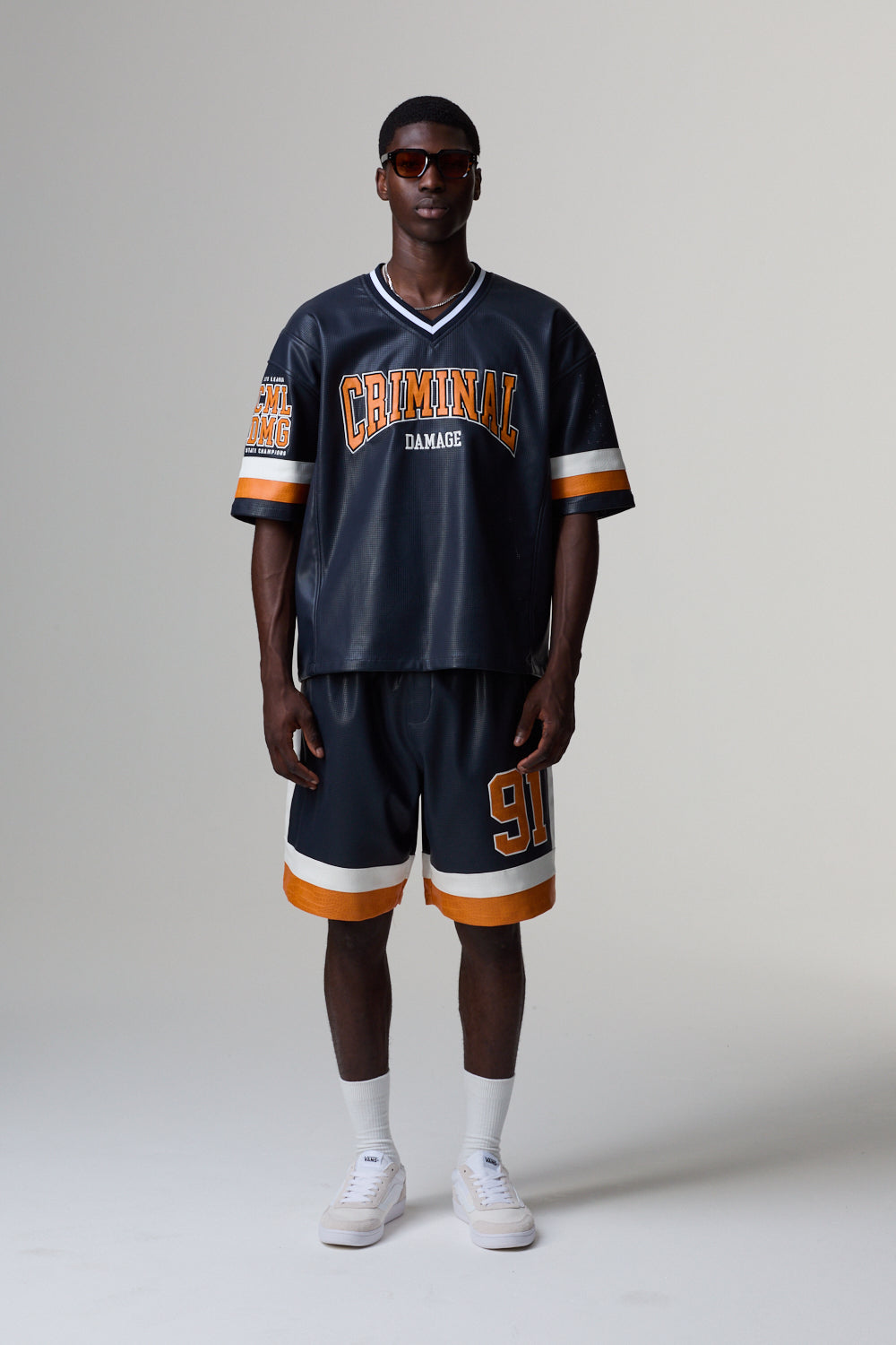 Model wearing a Criminal Damage navy blue sports jersey with orange and white accents on a grey background