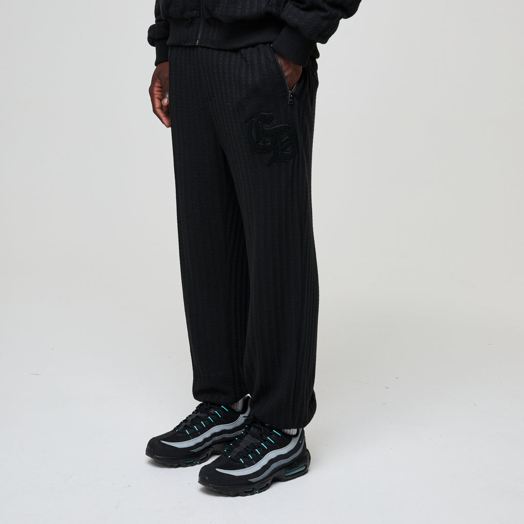 Person wearing black ribbed pants and black sneakers on a white background