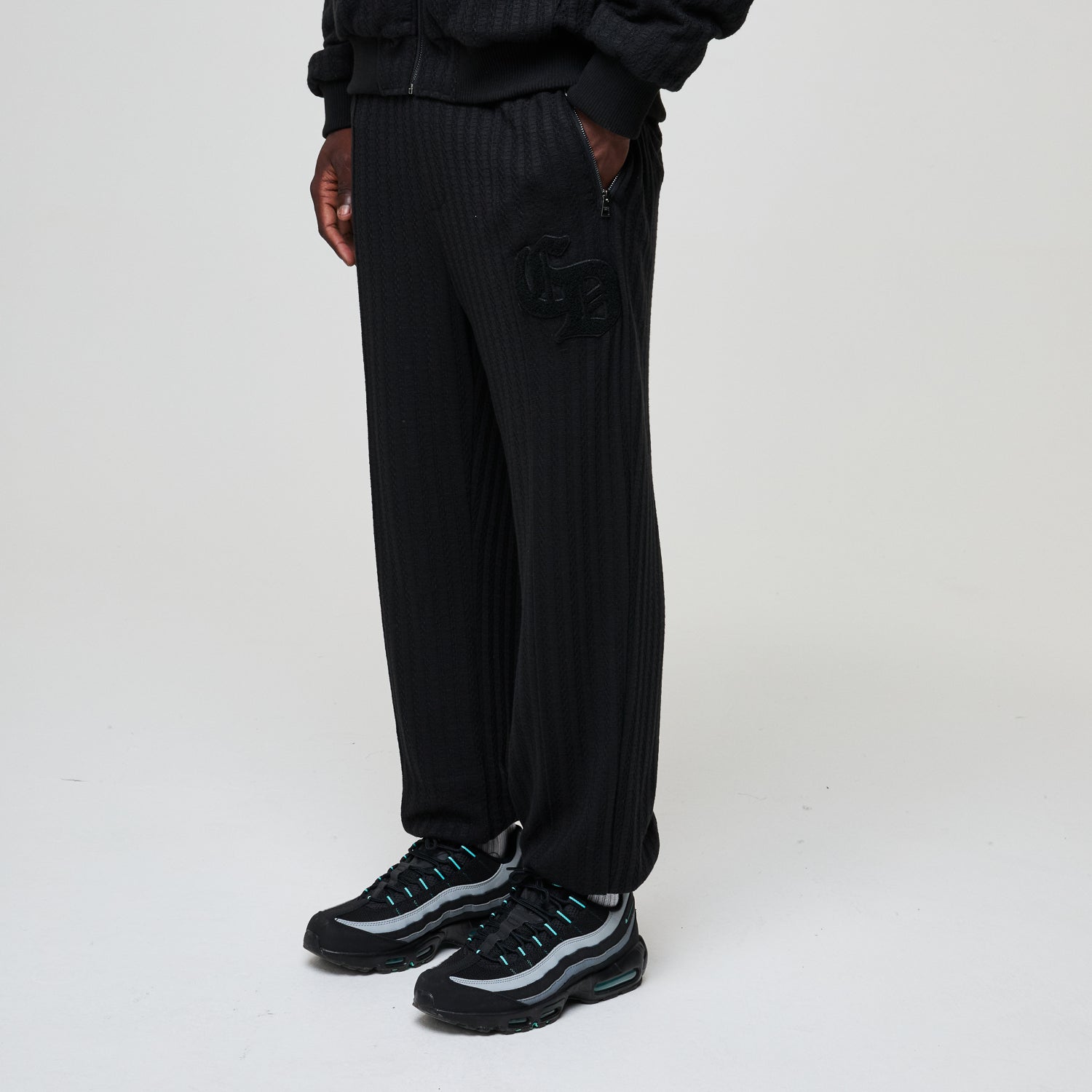 Person wearing black ribbed pants and black sneakers on a white background