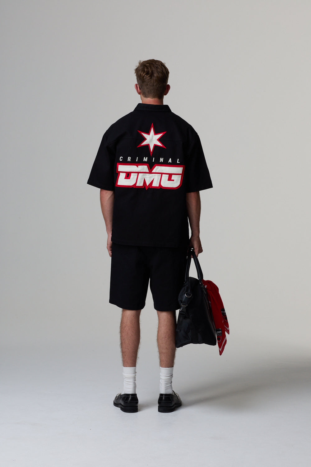 Person wearing a black shirt with 'CRIMINAL DMG' logo on the back, holding a red jacket.